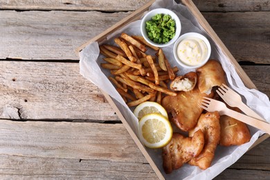 Photo of Tasty fish, chips, sauce and peas on wooden table, top view. Space for text