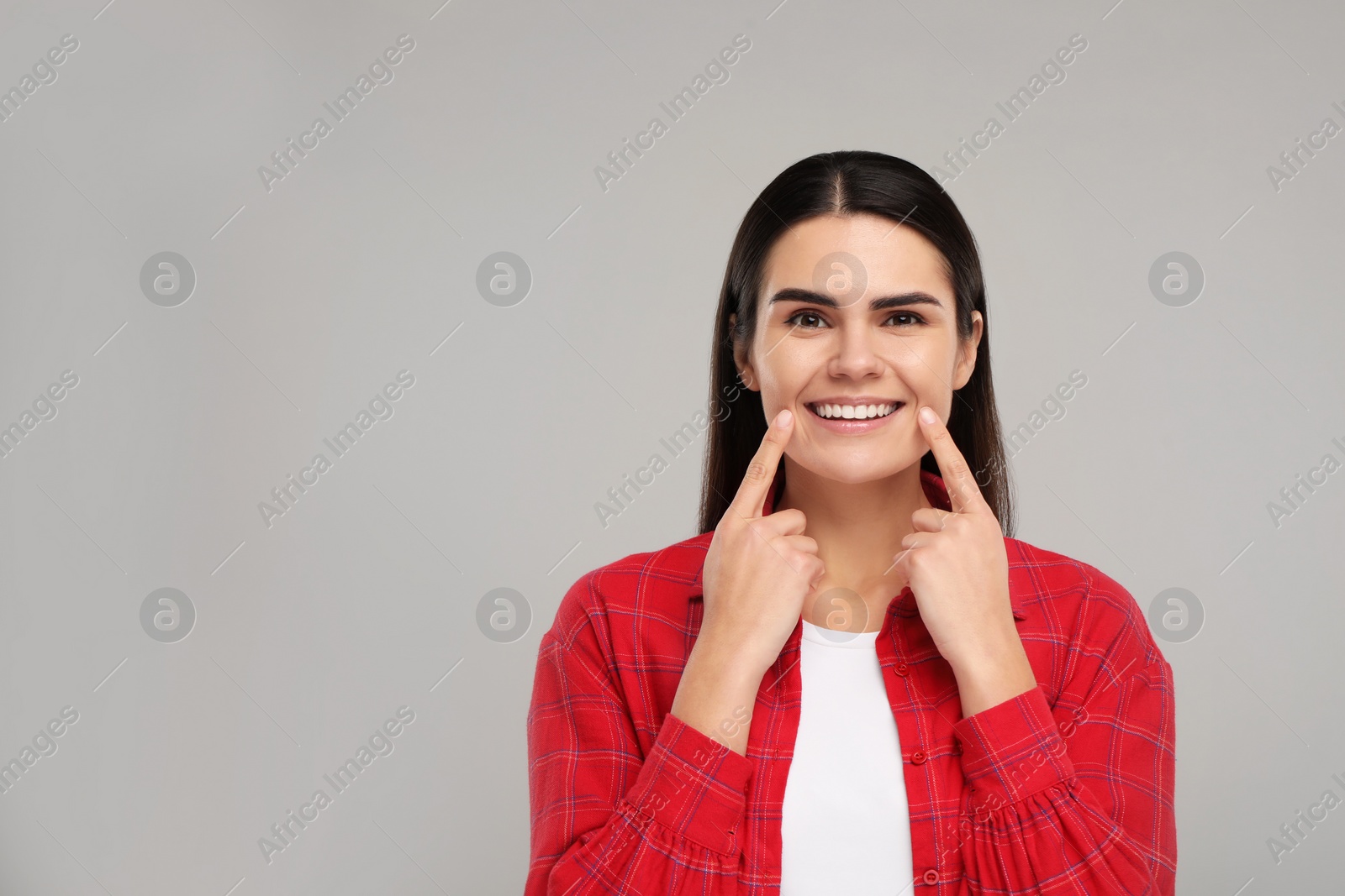 Photo of Young woman pointing at her clean teeth and smiling on light grey background, space for text