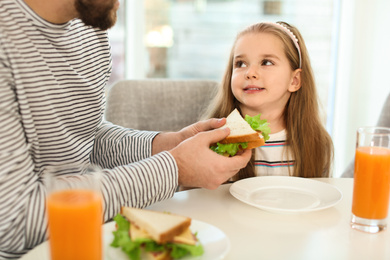 Photo of Father and daughter having breakfast with sandwiches at table in kitchen