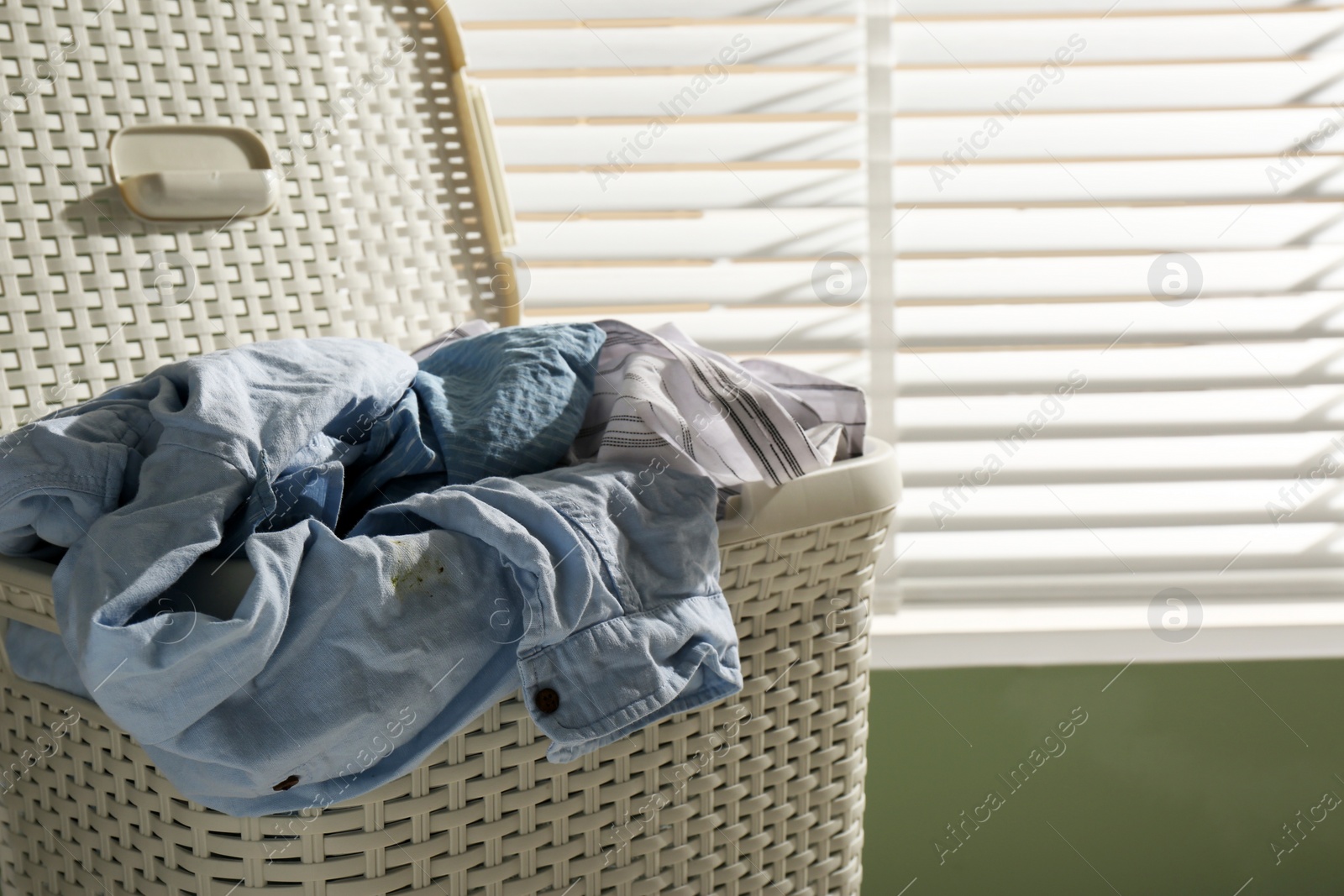 Photo of Laundry basket with clothes near window indoors, closeup. Space for text