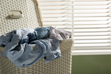 Laundry basket with clothes near window indoors, closeup. Space for text