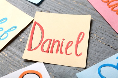 Paper sheet with baby name Daniel on grey wooden table, closeup