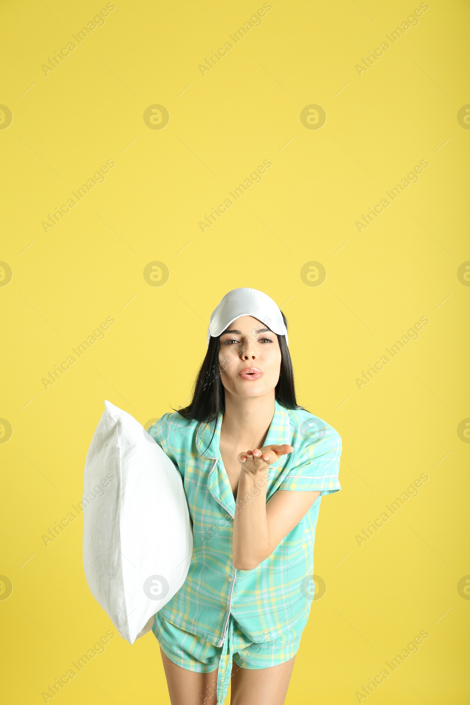 Photo of Young woman with pillow and sleep mask on yellow background