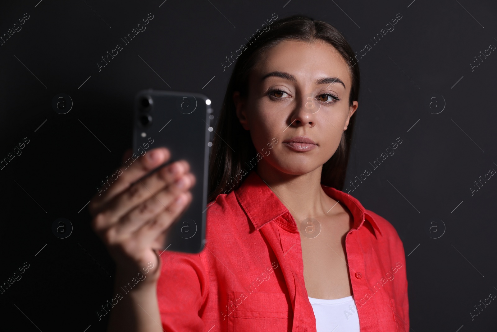 Photo of Young woman unlocking smartphone with facial scanner on black background. Biometric verification