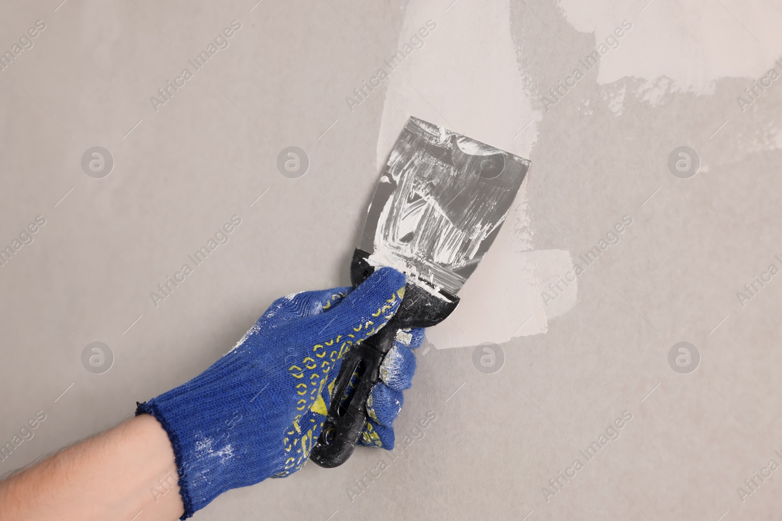 Photo of Worker plastering wall with putty knife indoors, closeup