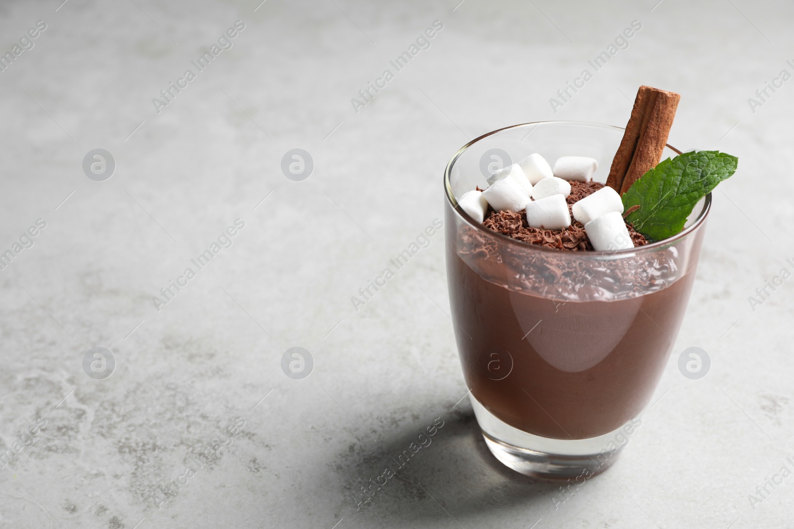 Photo of Cup of delicious hot chocolate with marshmallows, cinnamon stick and mint on light grey table, space for text