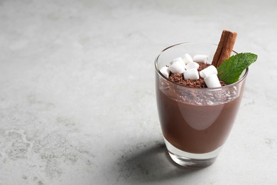Photo of Cup of delicious hot chocolate with marshmallows, cinnamon stick and mint on light grey table, space for text