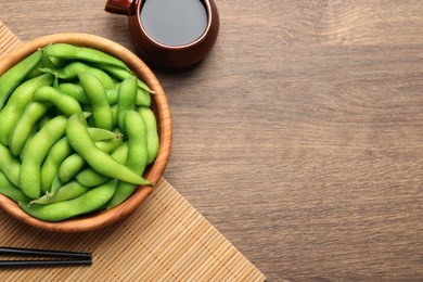 Photo of Green edamame beans in pods served with soy sauce on wooden table, flat lay. Space for text
