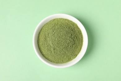 Photo of Wheat grass powder in bowl on green table, top view
