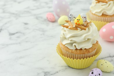 Photo of Tasty Easter cupcake with vanilla cream and candies on white marble table, space for text