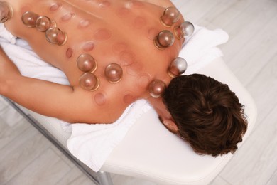 Photo of Cupping therapy. Man with glass cups on massage couch indoors, top view