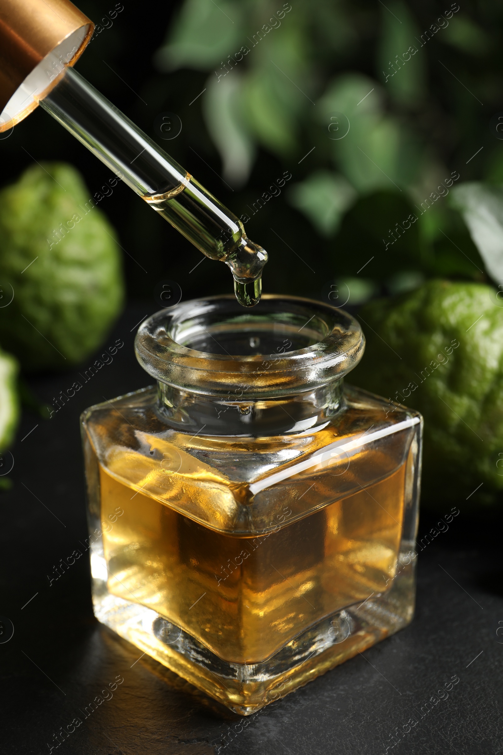 Photo of Dripping bergamot essential oil into glass bottle on black stone table