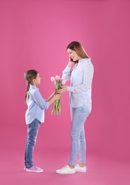 Happy mother and daughter with flowers on color background. International Women's Day