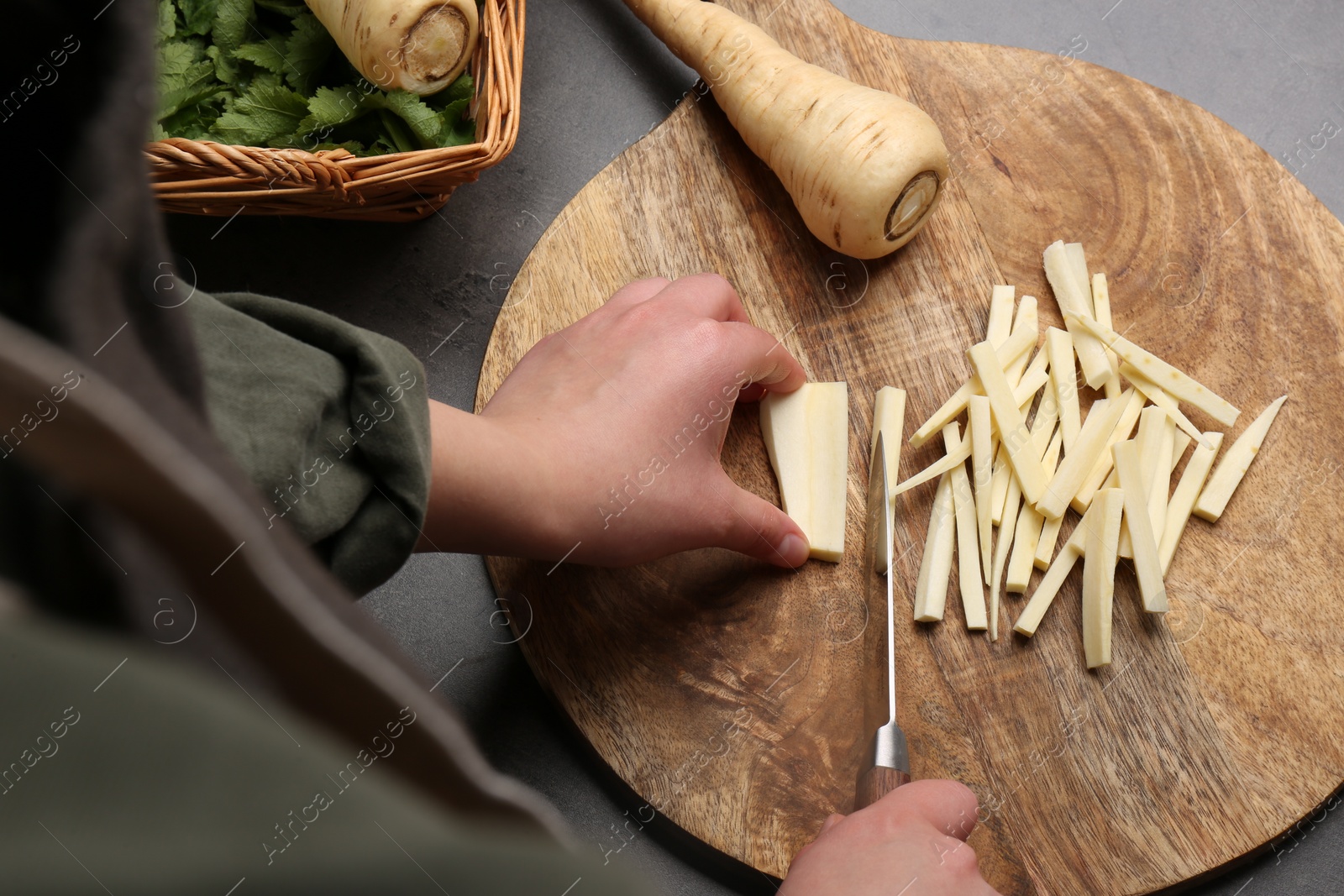 Photo of Woman cutting delicious fresh ripe parsnip at black table, above view