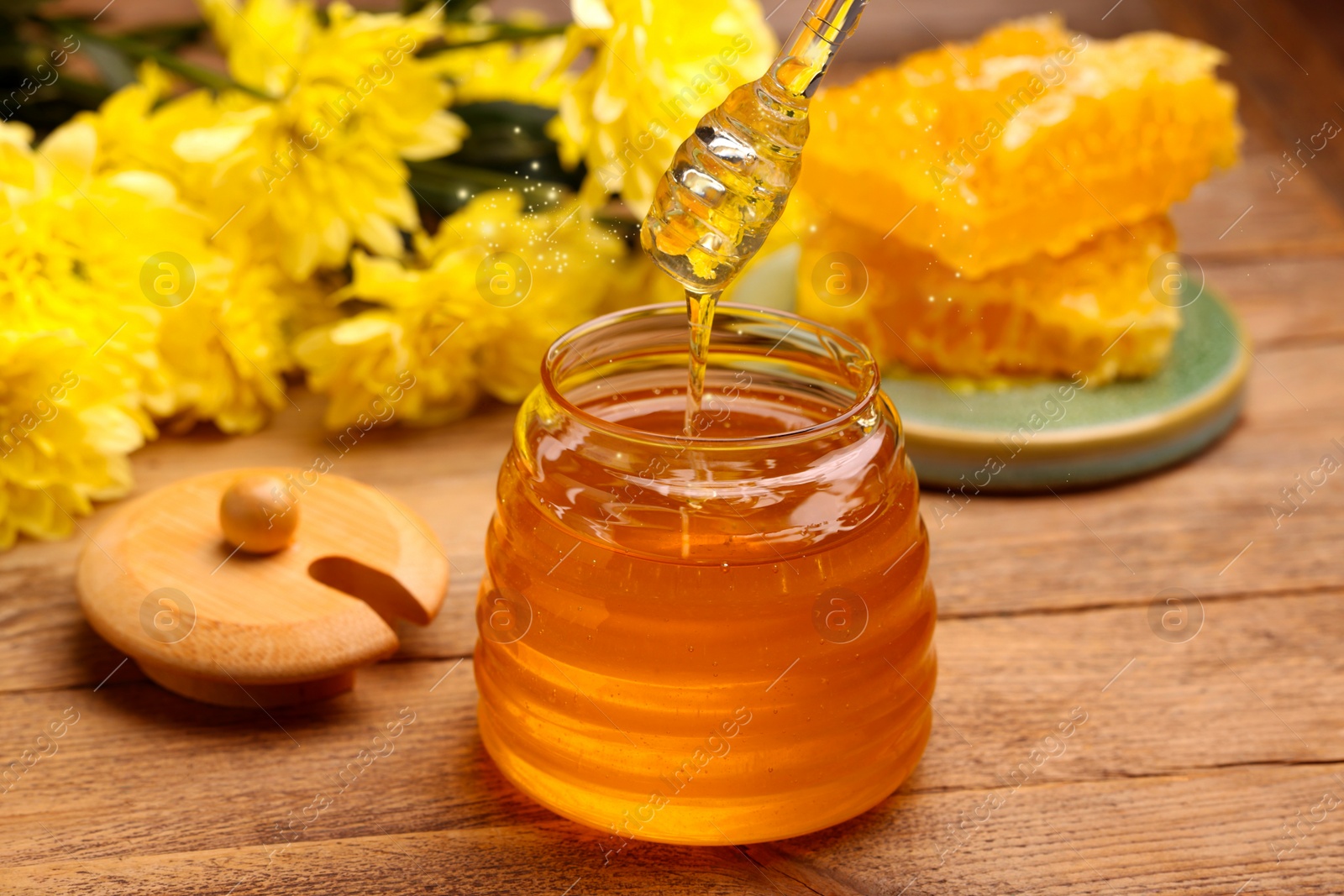 Image of Natural honey in glass jar and dipper on wooden table under sunlight