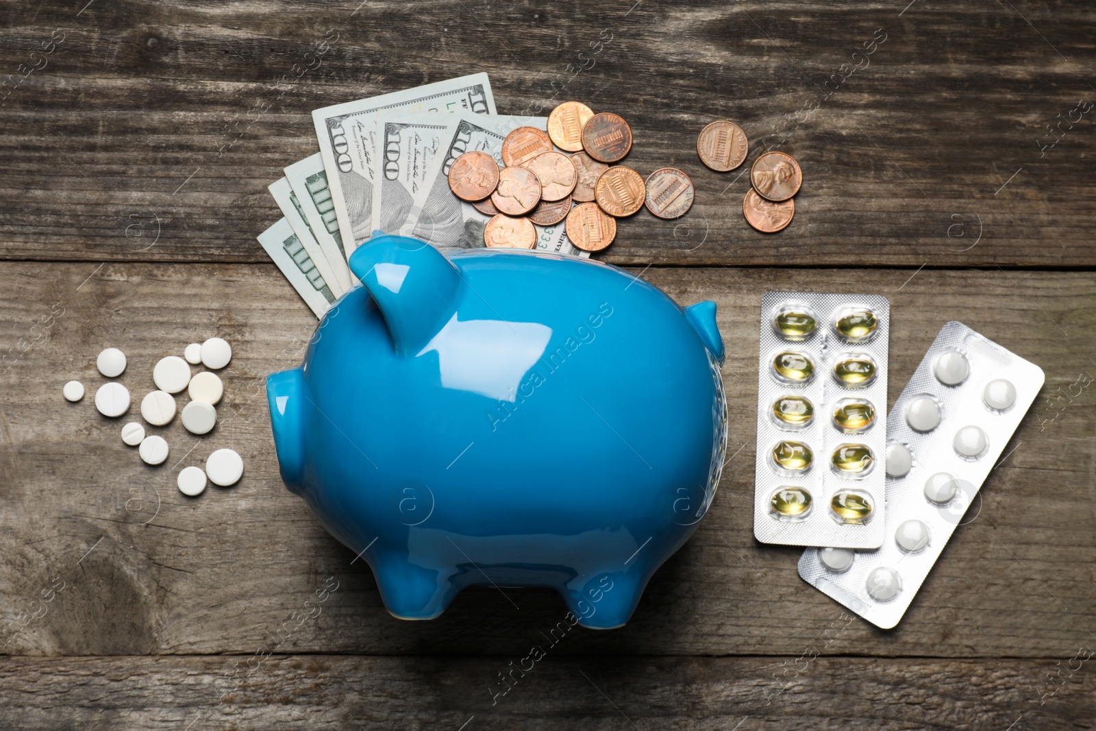 Photo of Light blue ceramic piggy bank, money and pills on wooden table, flat lay. Medical insurance