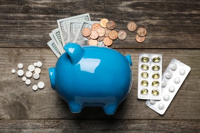 Light blue ceramic piggy bank, money and pills on wooden table, flat lay. Medical insurance