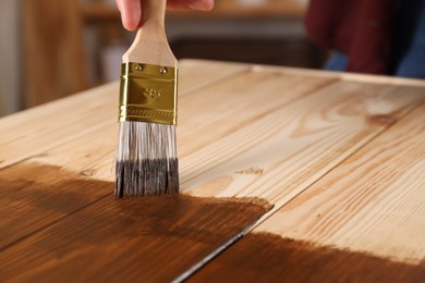 Man with brush applying wood stain onto wooden surface, closeup. Space for text