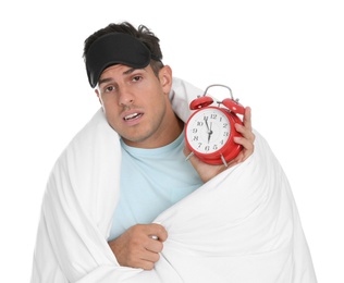 Man in sleeping mask wrapped with blanket holding alarm clock on white background