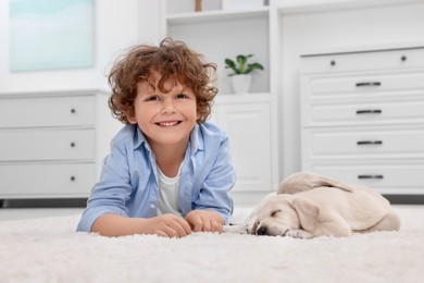 Photo of Little boy lying with cute puppies on white carpet at home