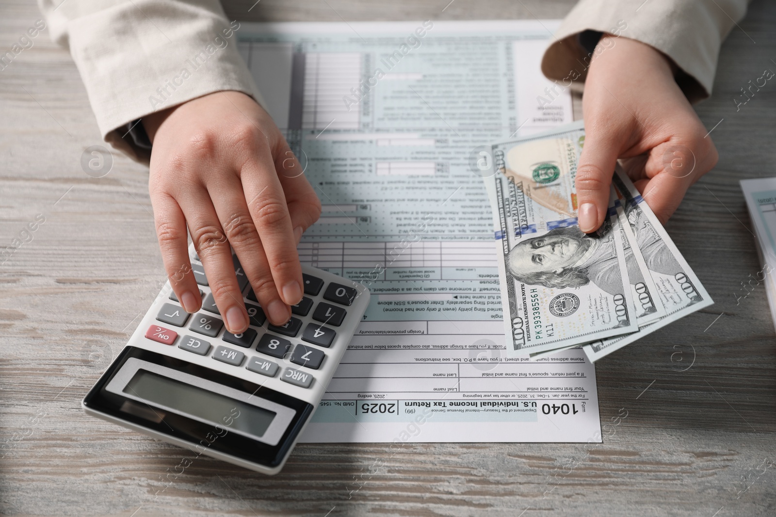 Photo of Payroll. Woman with dollar banknotes and calculator planning budget at wooden table, closeup