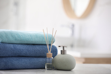 Photo of Stack of fresh towels, reed air freshener and soap dispenser on table in bathroom