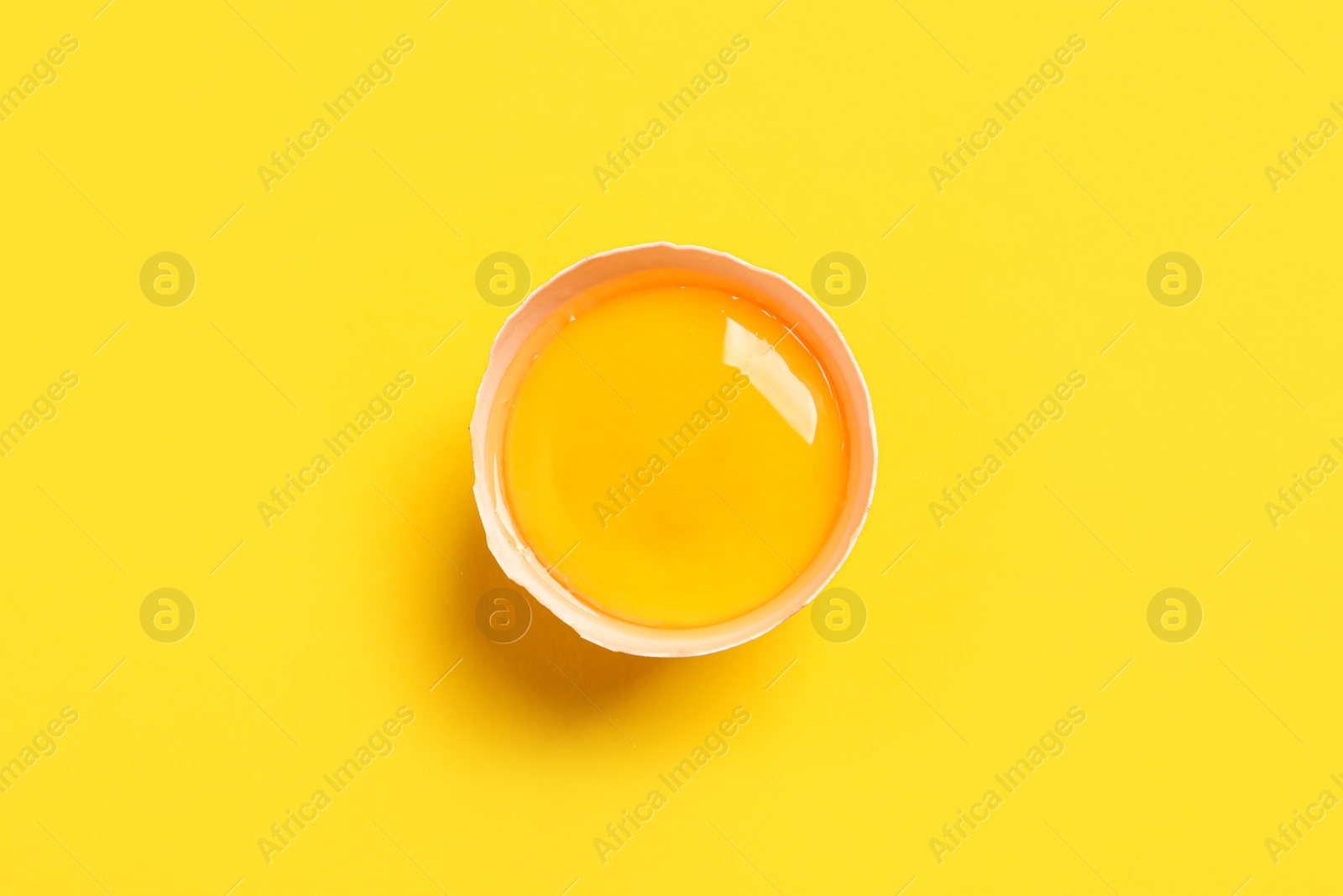 Photo of Cracked eggshell with raw yolk on yellow background, top view