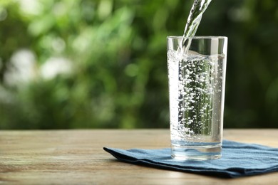 Photo of Pouring water into glass on wooden table outdoors, space for text