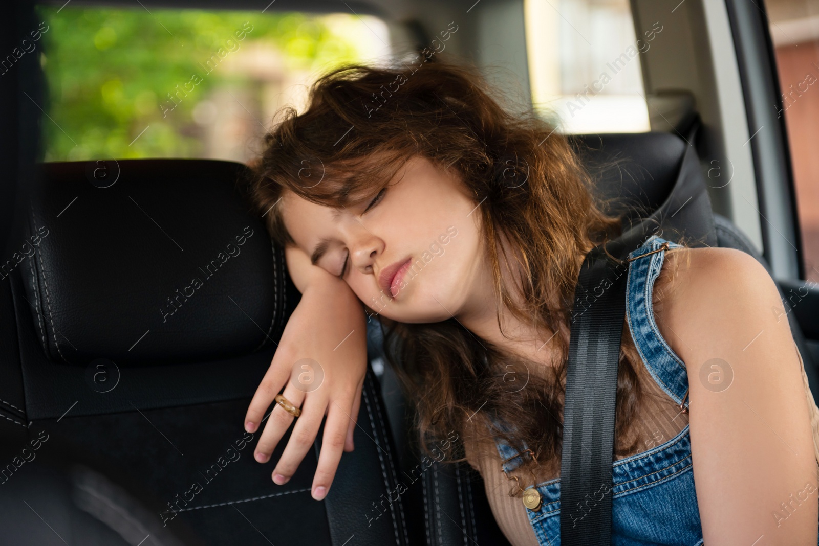 Photo of Tired girl with fastened seat belt sleeping in car