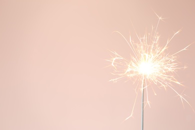 Photo of Bright burning sparkler on pink background, closeup. Space for text
