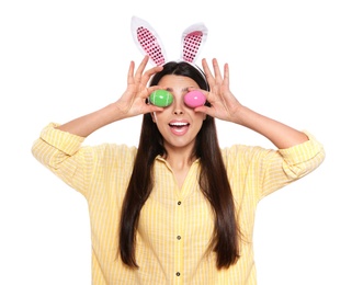 Photo of Beautiful woman in bunny ears headband holding Easter eggs near eyes on white background