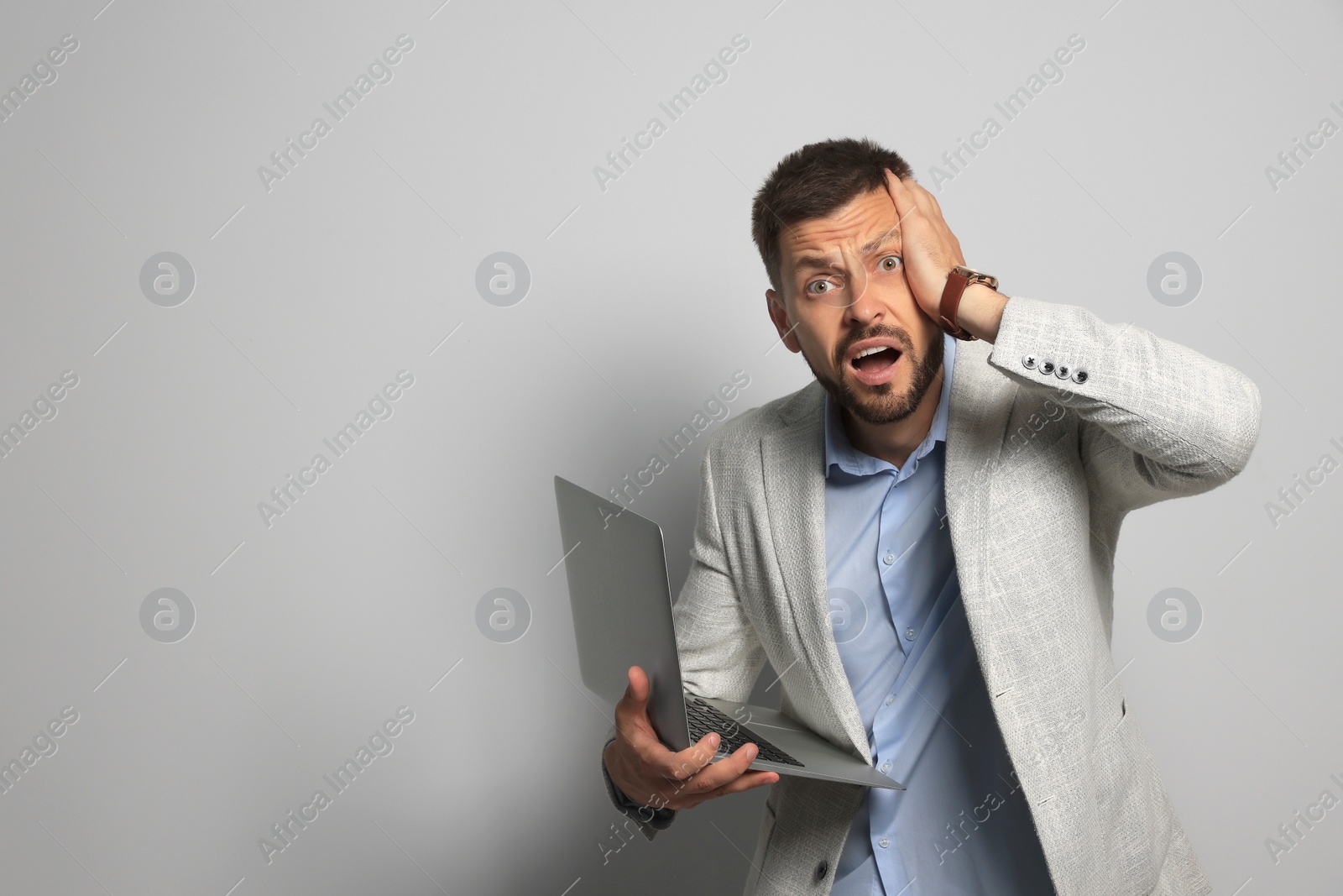 Photo of Emotional man with laptop on grey background, space for text. Being late concept