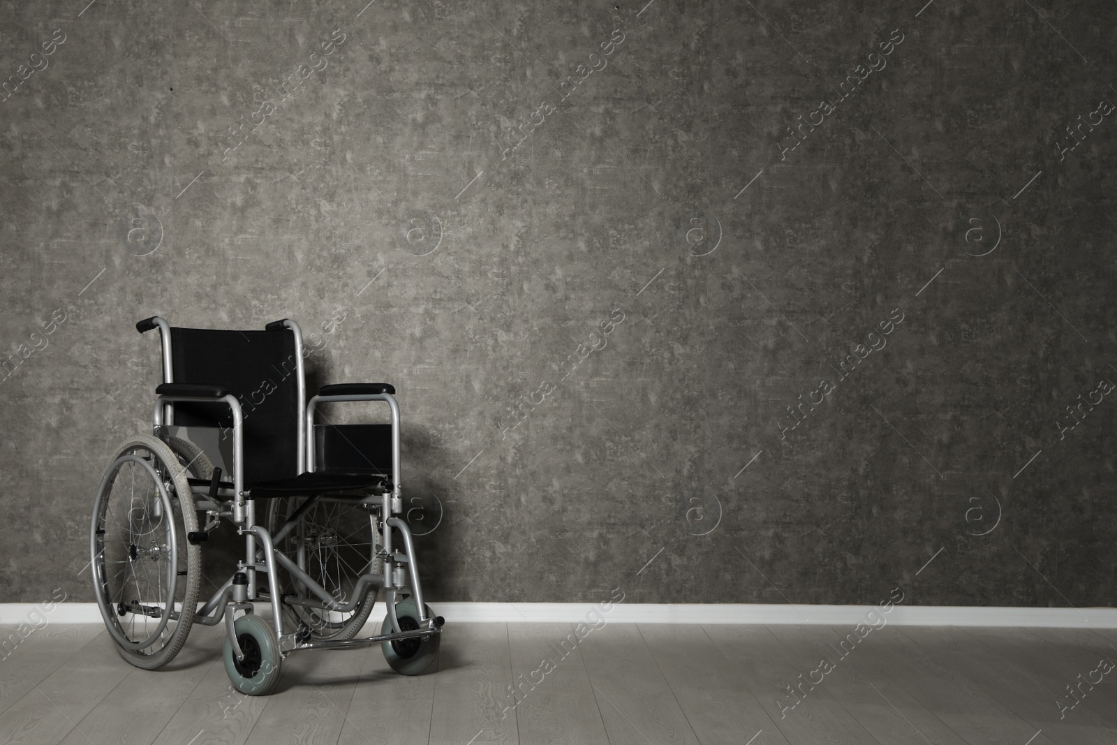 Photo of Empty wheelchair near grey wall indoors. Space for text