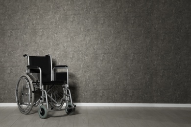 Empty wheelchair near grey wall indoors. Space for text