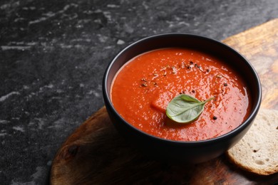 Delicious tomato cream soup in bowl on dark textured table, closeup. Space for text