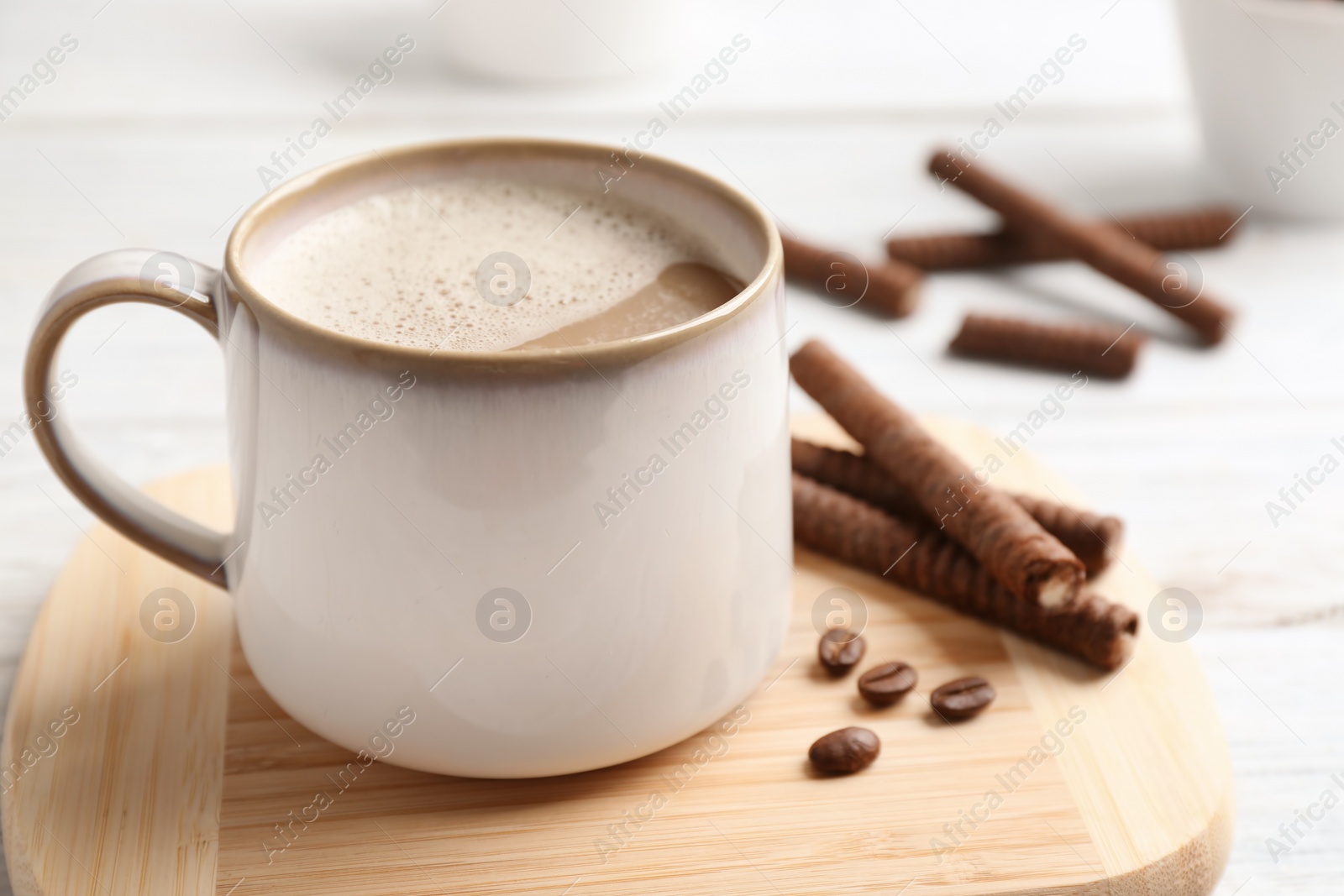 Photo of Delicious chocolate wafer rolls and cup of coffee on wooden board, closeup