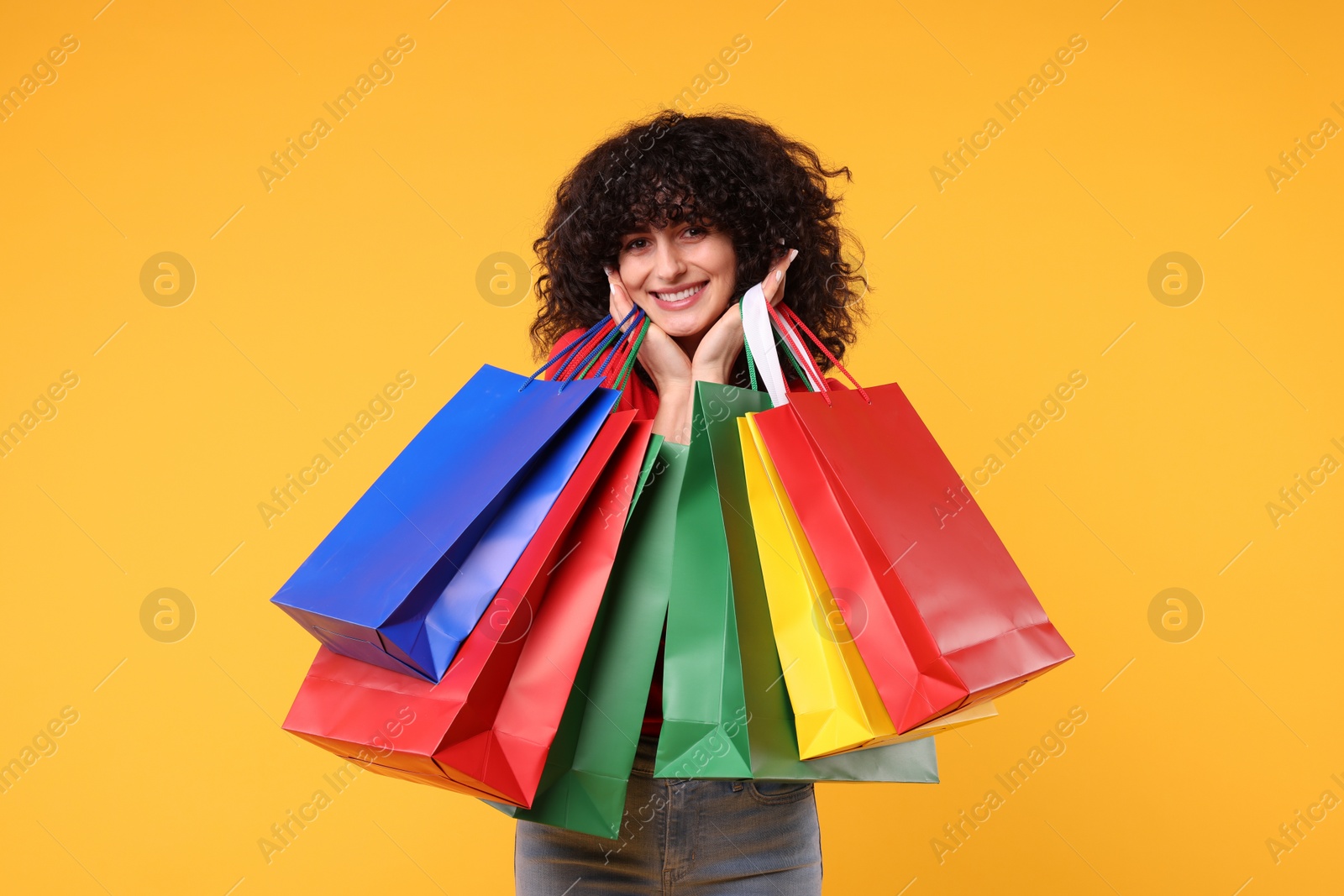 Photo of Happy young woman with shopping bags on yellow background