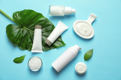 Different skin care cosmetic products with green leaves on color background, top view