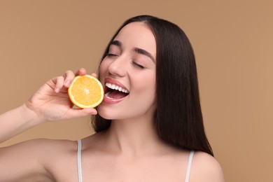 Beautiful young woman with piece of orange on beige background