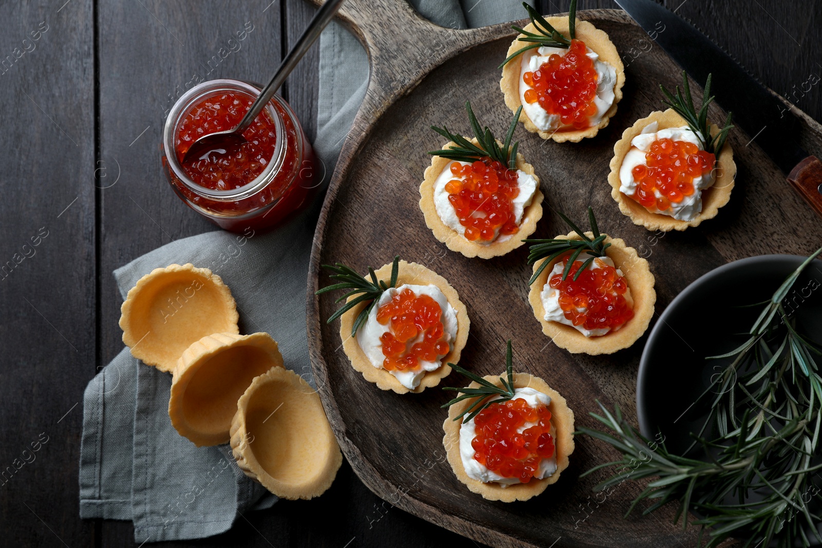 Photo of Delicious tartlets with red caviar and cream cheese served on wooden table, flat lay