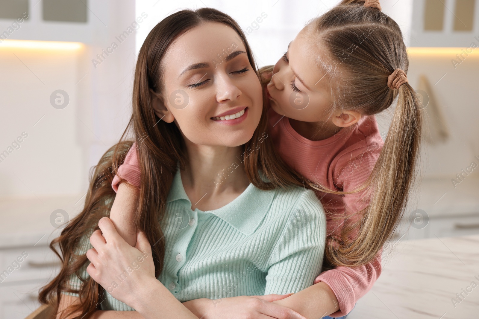 Photo of Cute daughter kissing her mom in kitchen