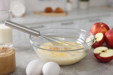 Photo of Whisk, bowl, beaten eggs and other ingredients on grey table indoors