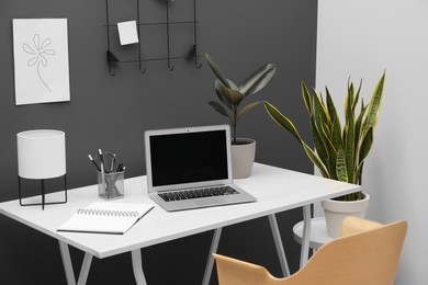 Photo of Cozy workplace with modern laptop on desk and comfortable chair at home