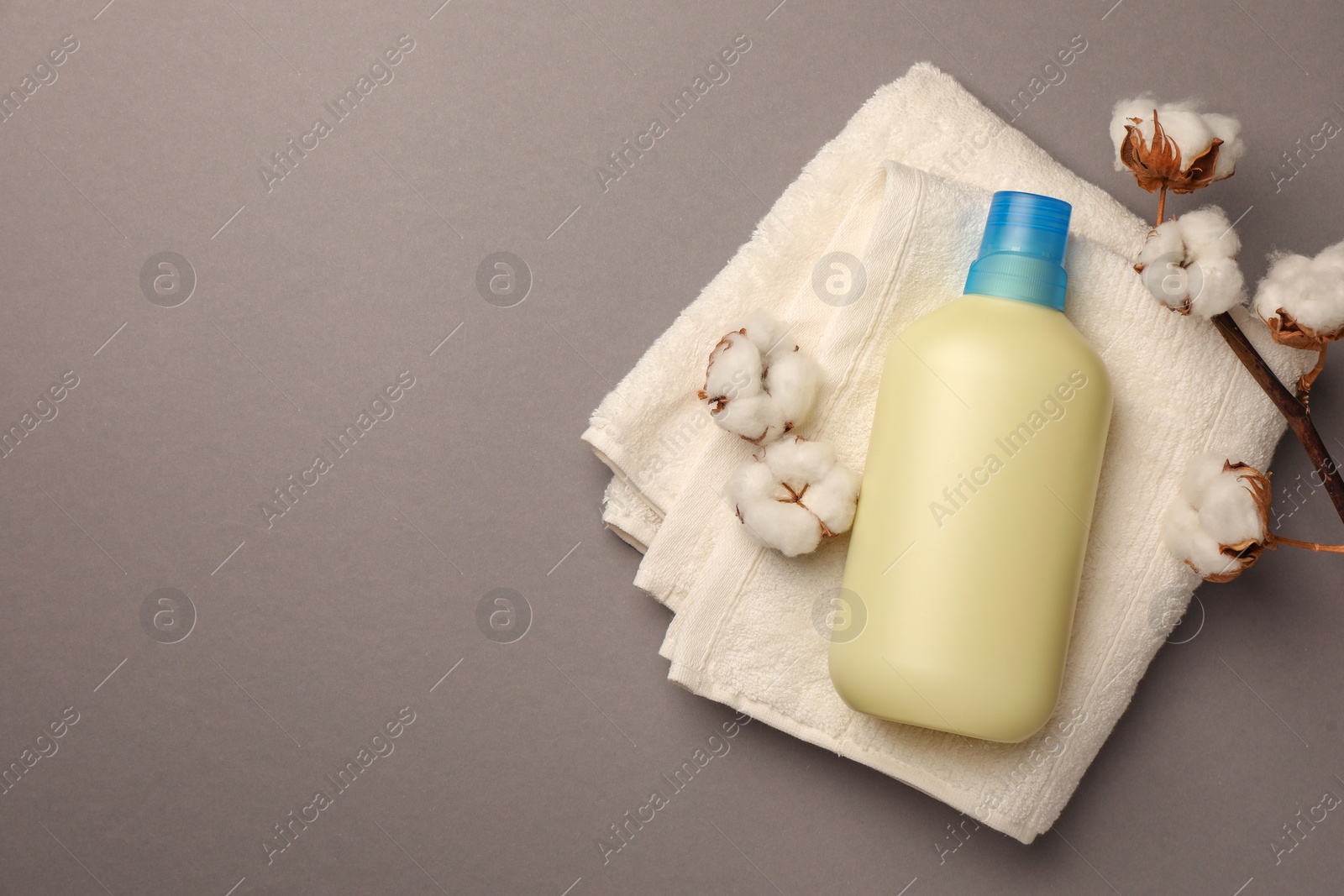 Bottle of fabric softener, terry towel and beautiful cotton flowers on gray background, top view. Space for text Photo of Bottle of fabric softener, terry towel and beautiful cotton flowers on gray background, top view. Space for text