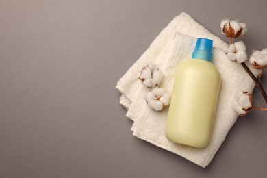 Photo of Bottle of fabric softener, terry towel and beautiful cotton flowers on gray background, top view. Space for text
