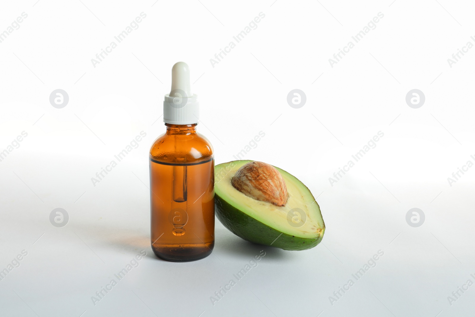 Photo of Bottle with oil and half of ripe fresh avocado on white background