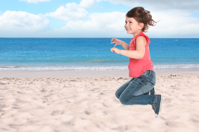 Image of Happy school girl jumping on beach near sea, space for text. Summer holidays