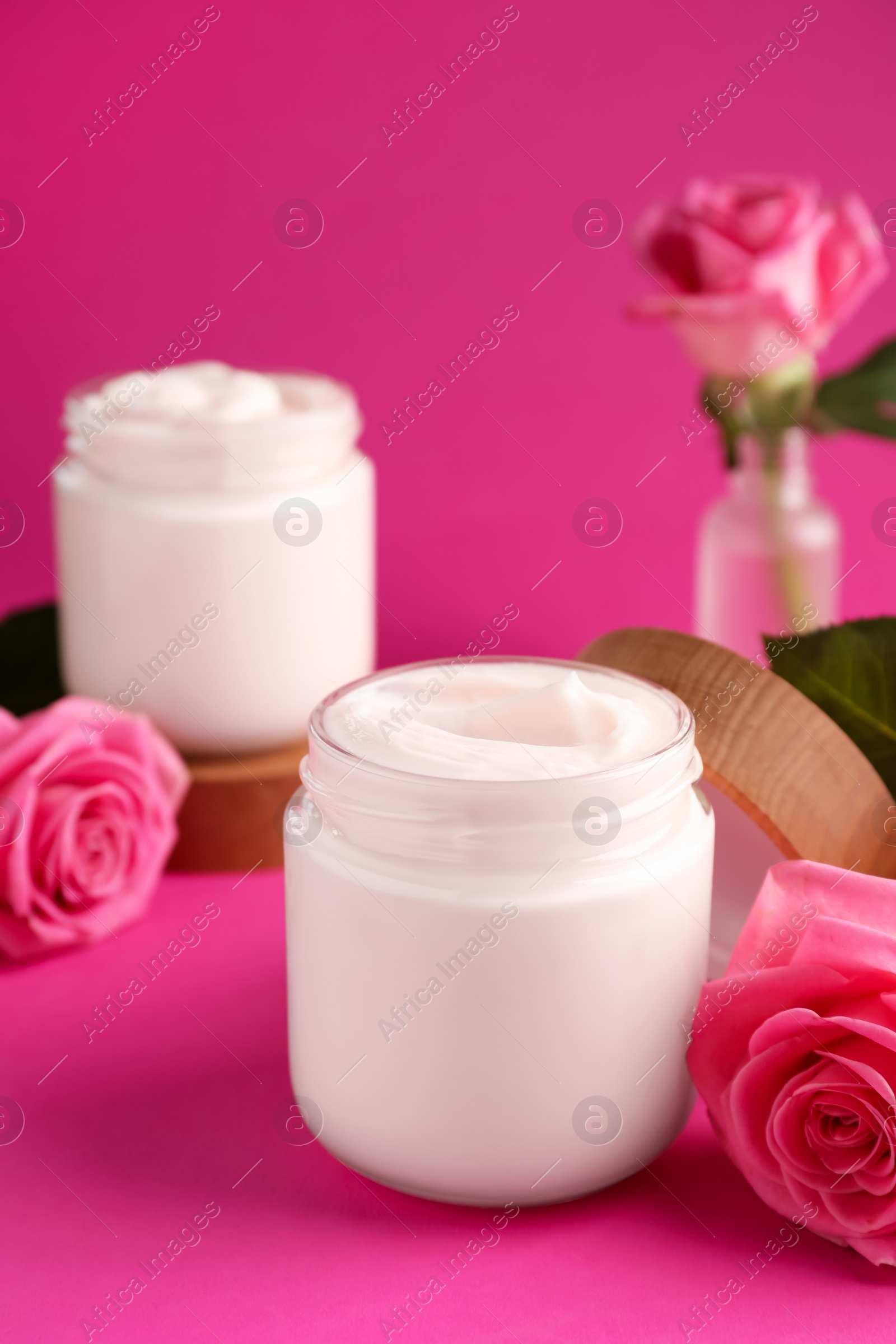 Photo of Glass jars of face cream and roses on pink background