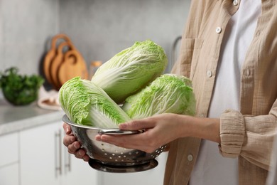 Photo of Woman holding fresh chinese cabbages in kitchen, closeup