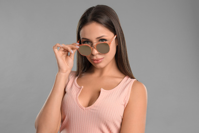 Beautiful young woman wearing sunglasses on grey background
